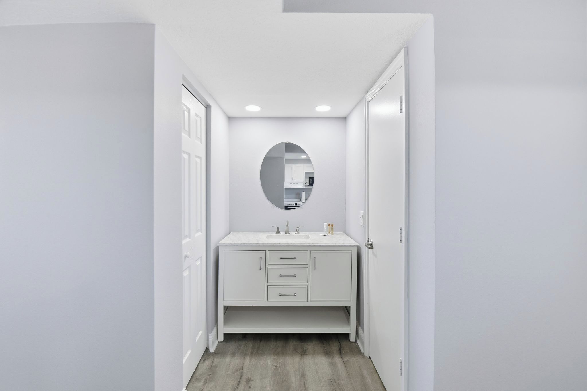 Un couloir étroit avec une coiffeuse blanche, un miroir et des spots encastrés.
