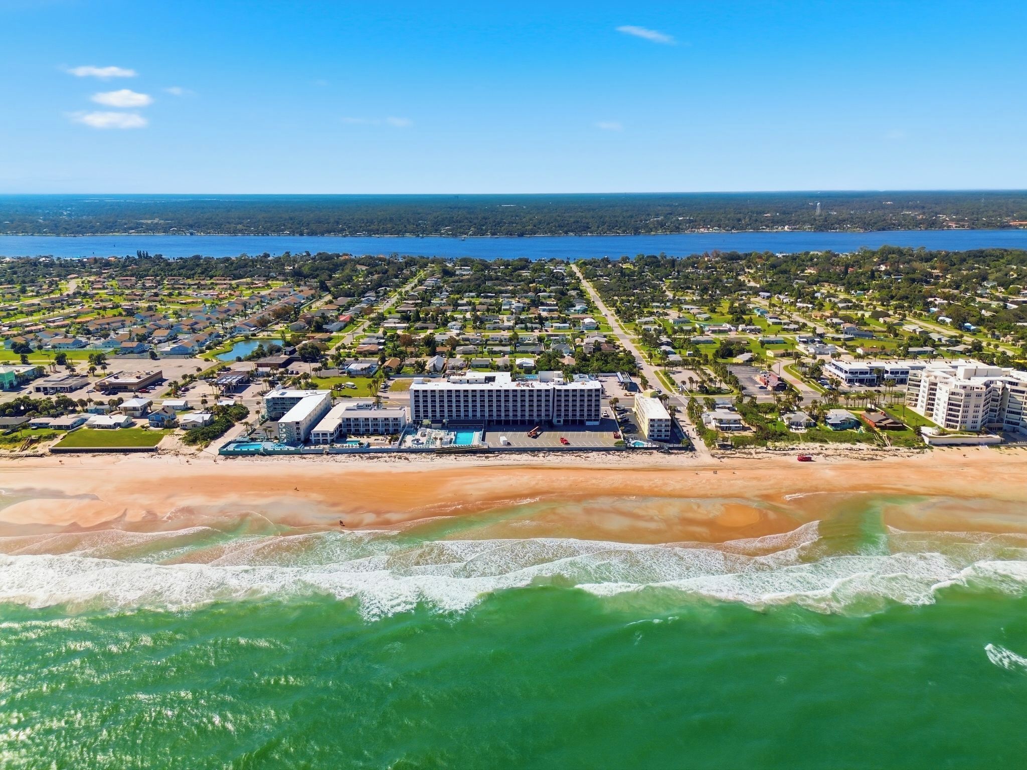 Vista aérea de un complejo turístico costero con un gran edificio hotelero, propiedades frente a la playa y un puerto deportivo.