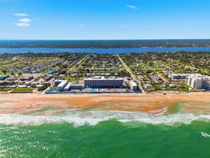 An aerial view of a coastal resort with a large hotel building, beachfront properties, and a marina. - The Maverick Resort (Ormond Beach)