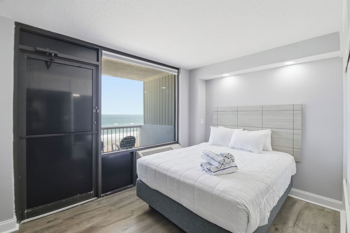Une chambre d’hôtel avec un lit, une grande fenêtre donnant sur un beau paysage, une porte coulissante et un balcon.