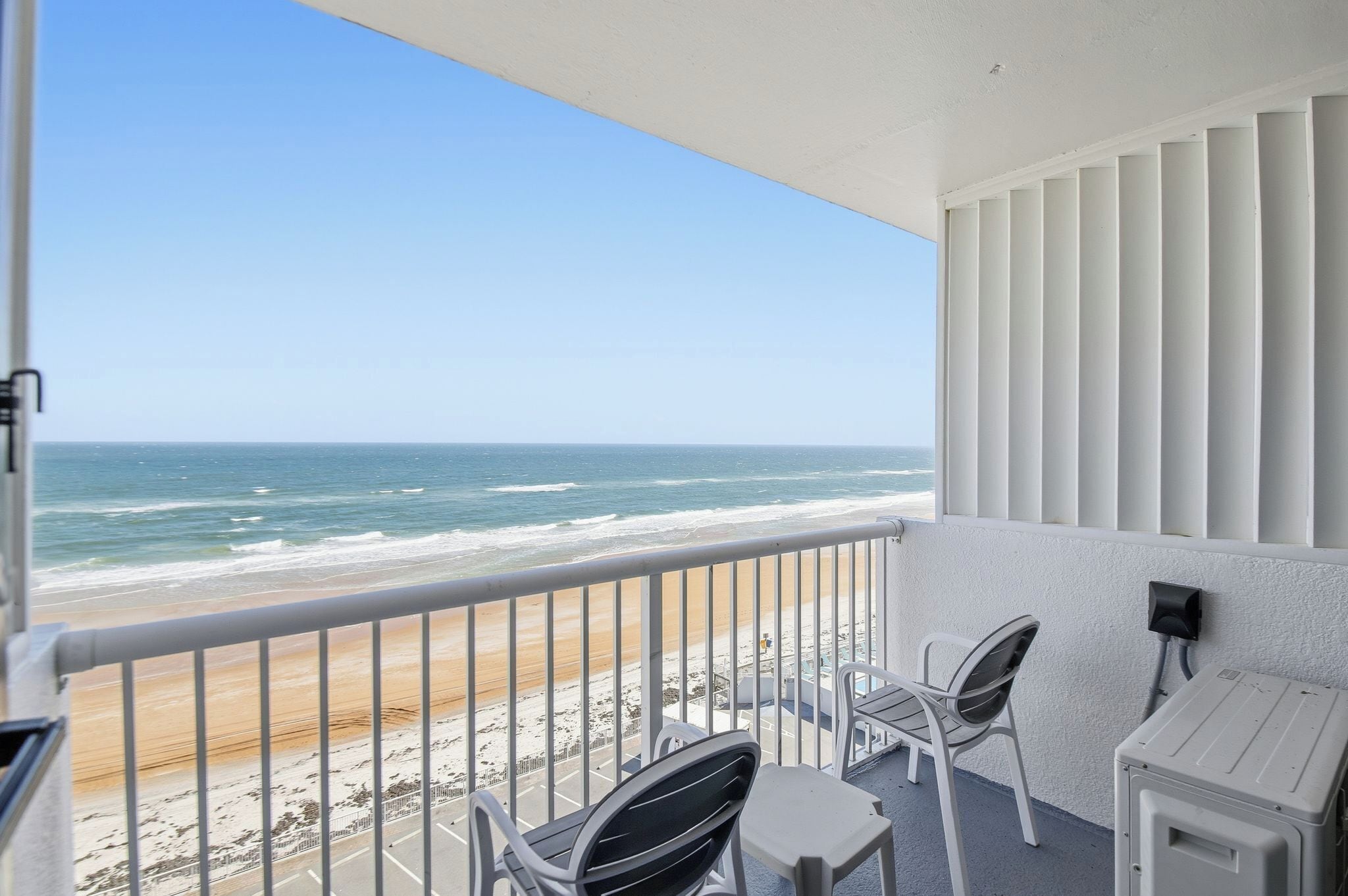 A balcony with a view of the beach and ocean. There are two chairs and a small table.