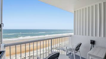 Un balcon avec vue sur la plage et l’océan. On y trouve deux chaises et une petite table.