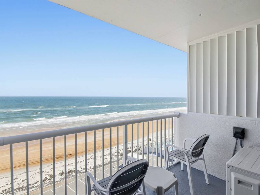 Un balcon avec vue sur la plage et l’océan. On y trouve deux chaises et une petite table.