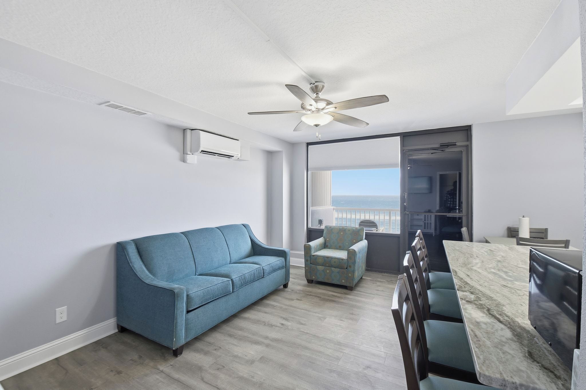 Una sala moderna con un sofá azul, un sillón estampado, una mesa de comedor y un ventilador de techo.