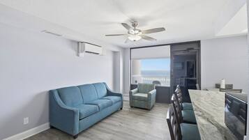 Una sala moderna con un sofá azul, un sillón estampado, una mesa de comedor y un ventilador de techo.