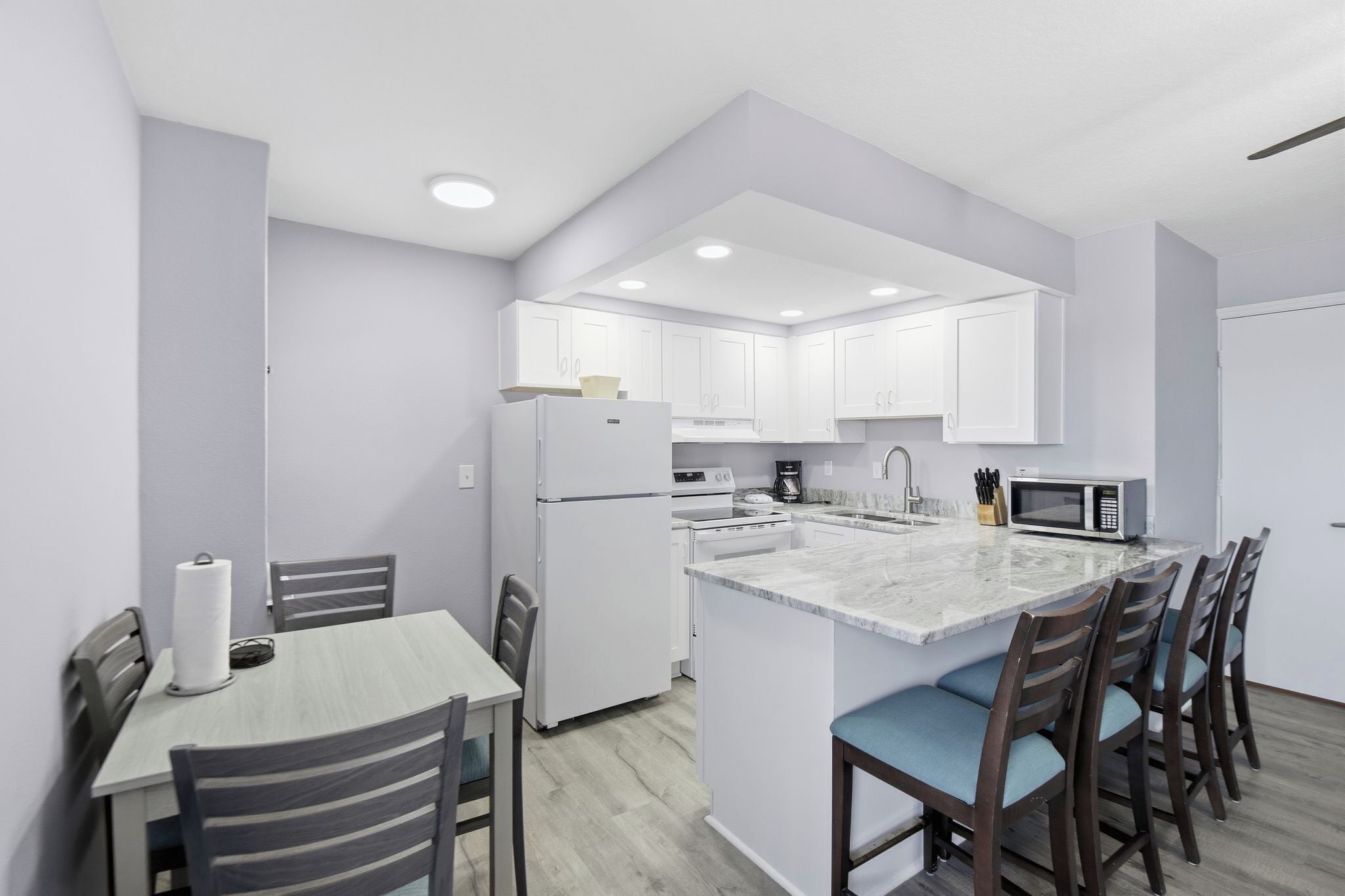 A modern kitchen with white cabinets, a marble island, and a dining area with striped chairs.