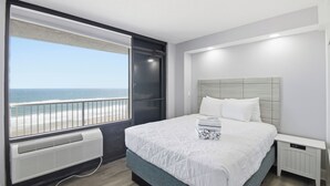 Una camera da letto con una grande finestra vista spiaggia, un letto con biancheria bianca e un comodino bianco.