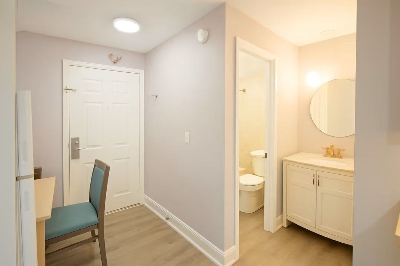 Un pasillo con una puerta, una silla y un baño con inodoro y lavamanos.