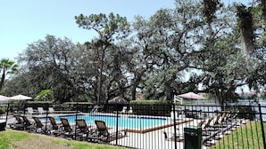 A swimming pool surrounded by lounge chairs and umbrellas, with trees and a fence in the foreground. - Lifetime of Vacations Resort (Kissimmee)
