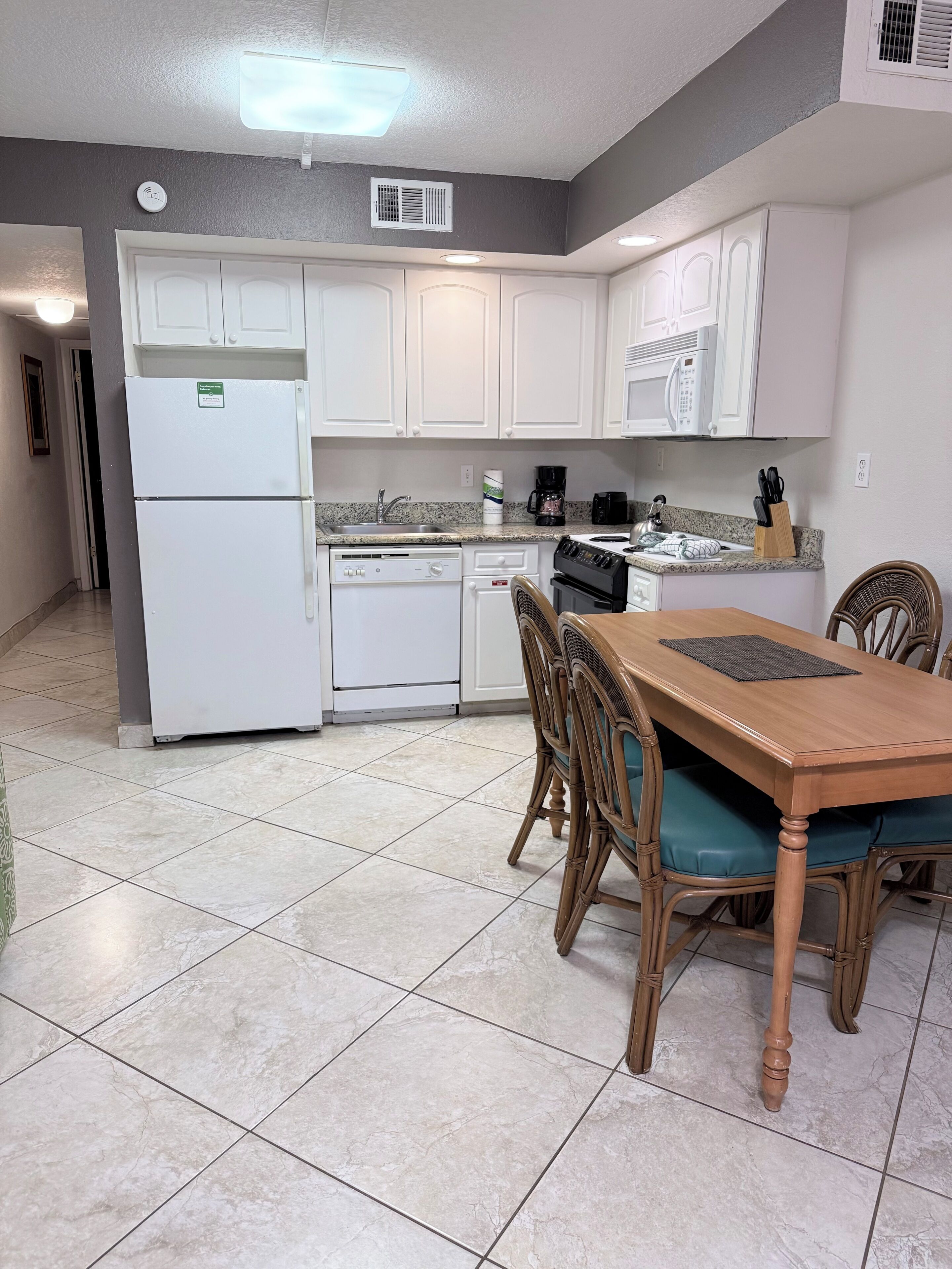 A kitchen with white cabinets, a refrigerator, a dishwasher, a microwave, and a dining table with chairs.