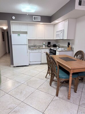 A kitchen with white cabinets, a refrigerator, a dishwasher, a microwave, and a dining table with chairs. - Lifetime of Vacations Resort (Kissimmee)