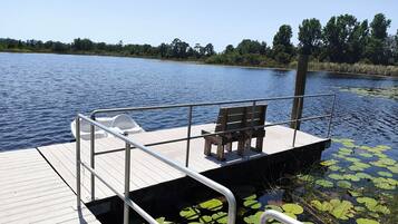 Un muelle de madera con un banco y un pequeño bote, rodeado de agua y nenúfares.