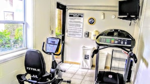 A fitness room with treadmills and an elliptical machine, a sign with exercise room rules, a clock, and a television on the wall. - Lifetime of Vacations Resort (Kissimmee)