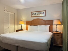 Habitación de hotel con una cama grande, dos mesitas de noche con lámparas, un cabecero de madera, un cuadro en la pared y un armario con puertas persianas.