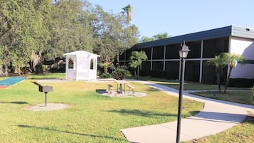 A courtyard with a small gazebo, a basketball court, and a building with a dark roof.