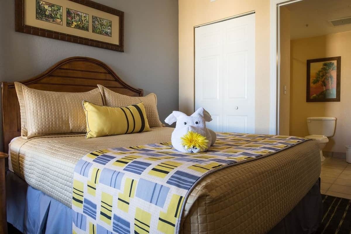 A neatly made bed with a quilt, pillows, and a stuffed toy on the bed.