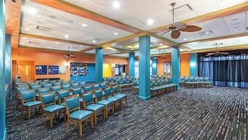 A large conference room with rows of chairs, a stage, and ceiling fans.