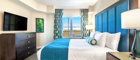 Une chambre d’hôtel avec un grand lit, un téléviseur à écran plat, une commode et une fenêtre avec des rideaux.