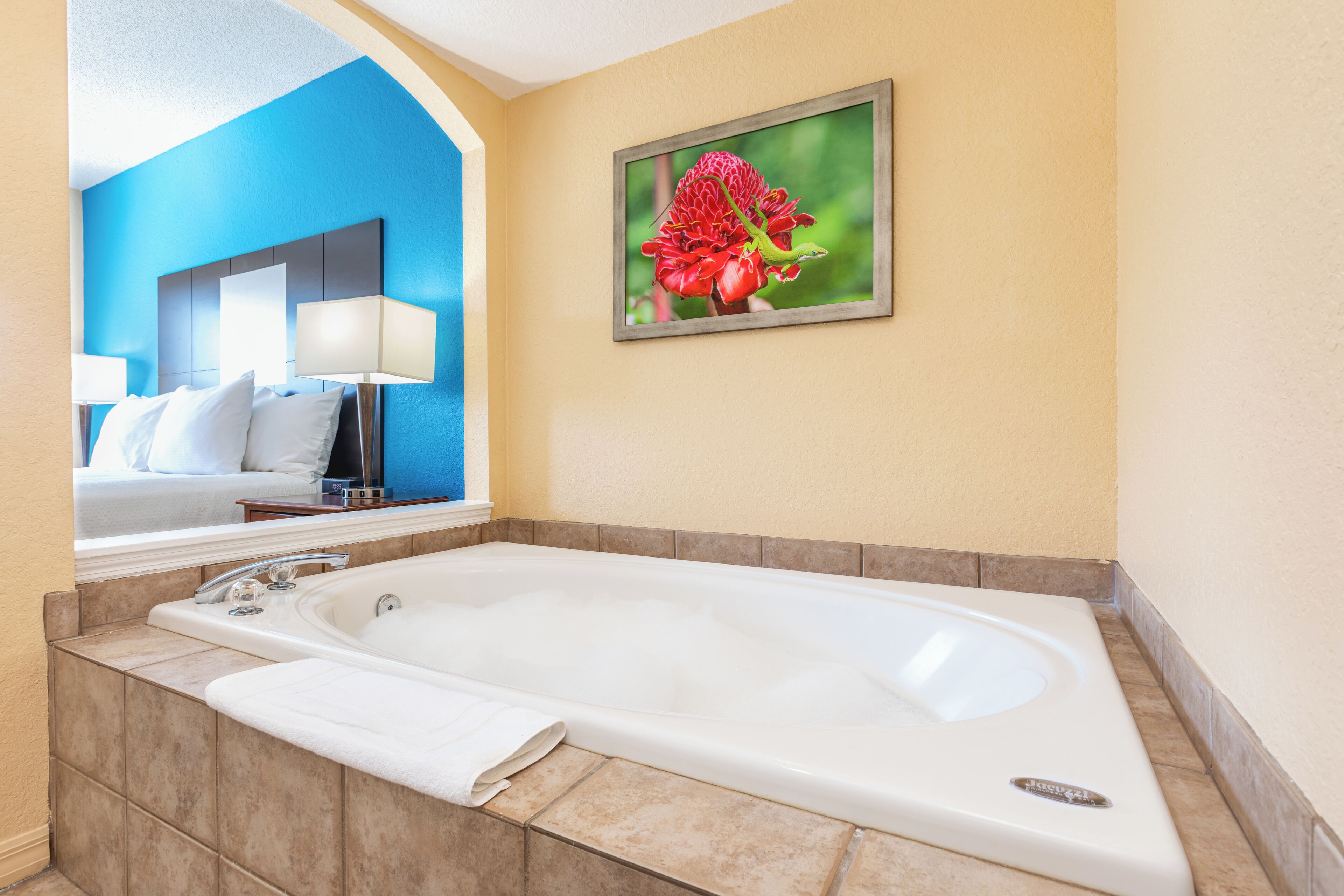 A hotel bathroom with a large bathtub, a mirror, and a framed picture of a flower on the wall.