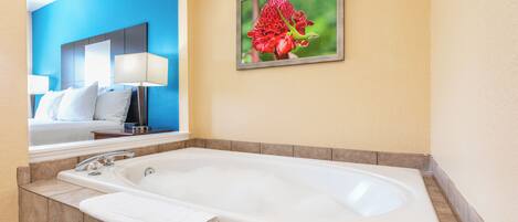 A hotel bathroom with a large bathtub, a mirror, and a framed picture of a flower on the wall.