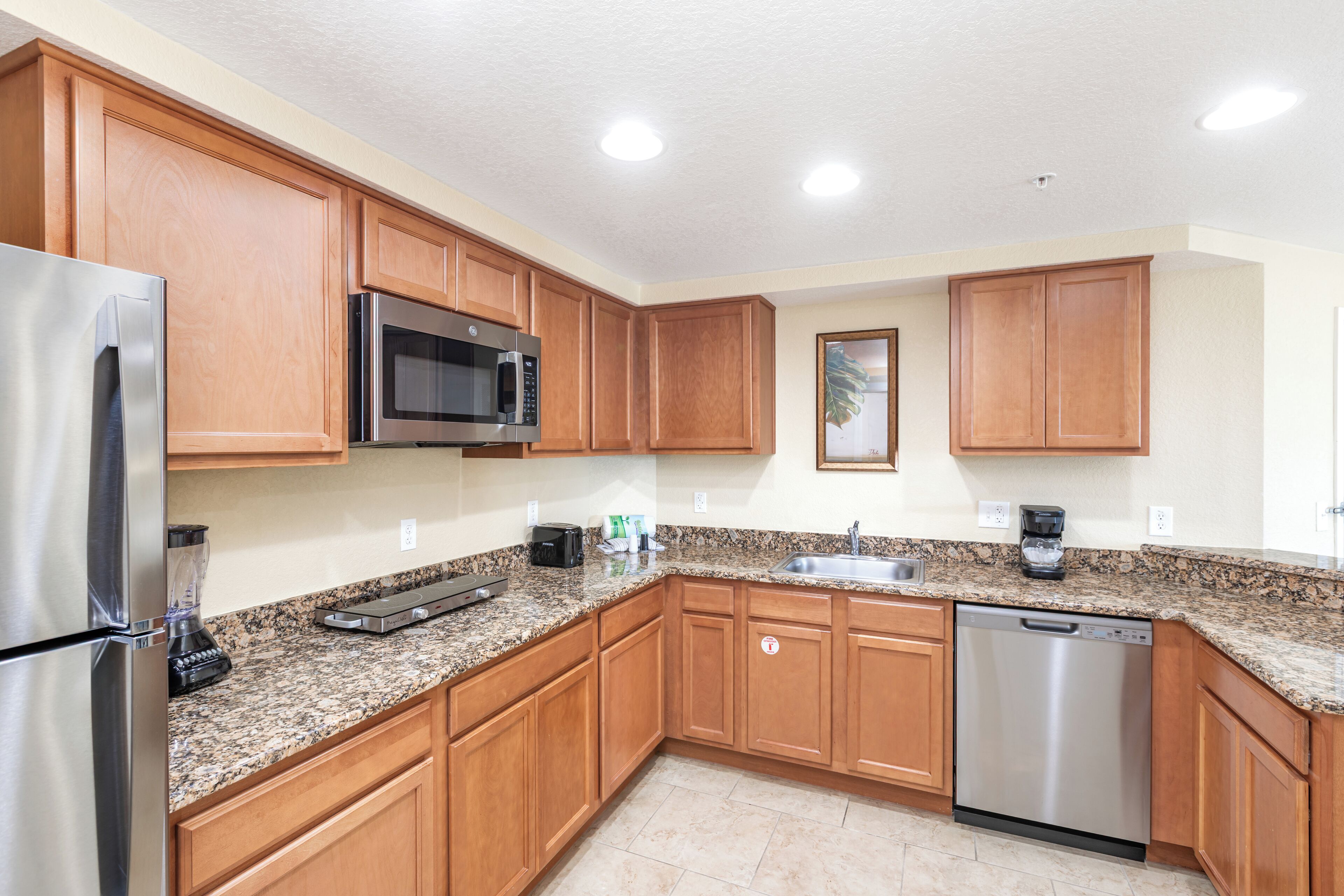 A kitchen with wooden cabinets, stainless steel appliances, granite countertops, and recessed ceiling lights.
