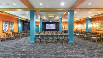 A conference room with rows of chairs, a large screen, and a carpeted floor.