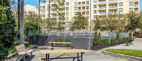 Une cour avec des tables de pique-nique et des bancs, entourée d’une clôture et de verdure.