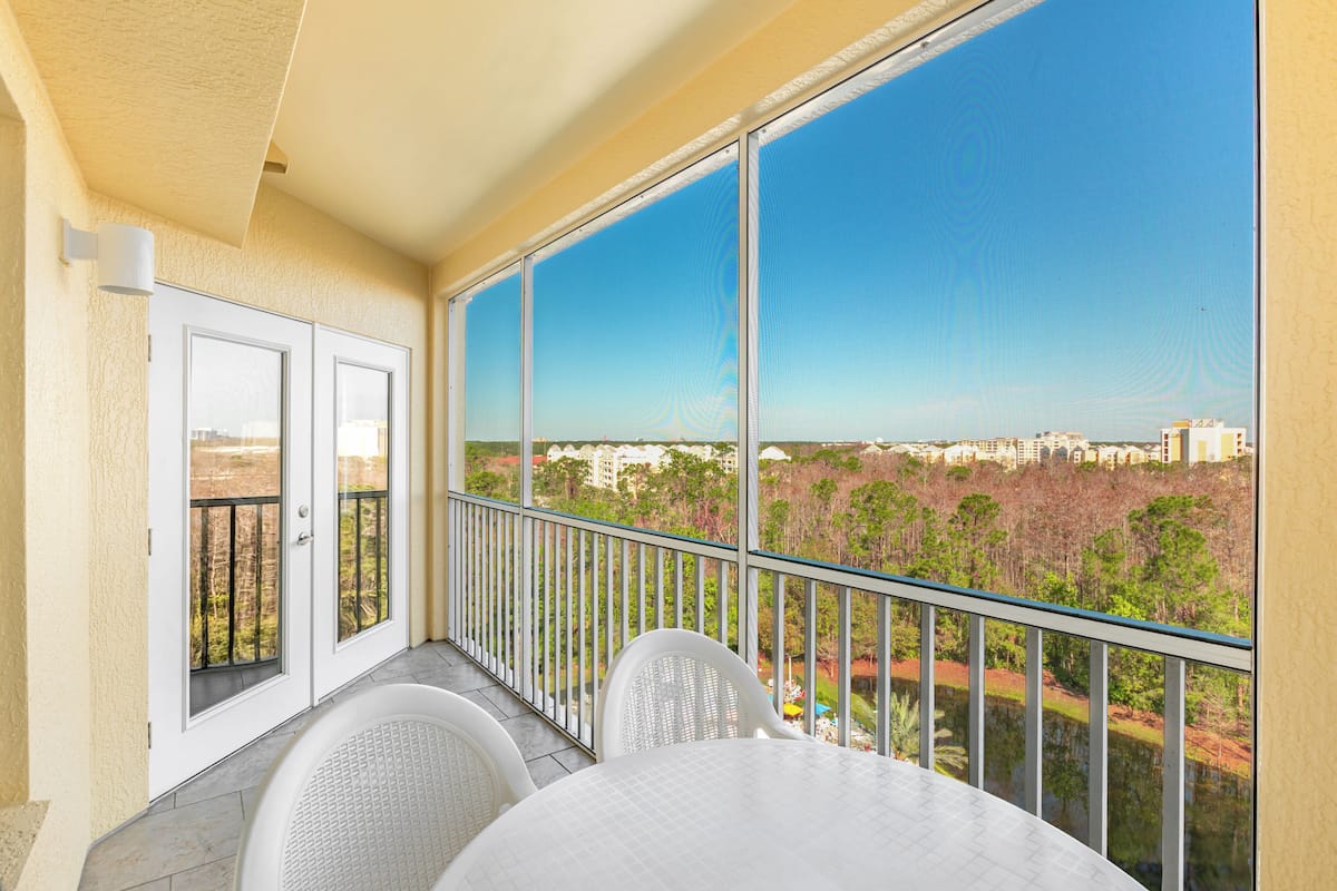 A balcony with a view of a cityscape, a white table, and two white chairs.