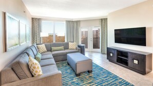 A modern living room with a sectional sofa, a flat-screen TV, and a large window with curtains.