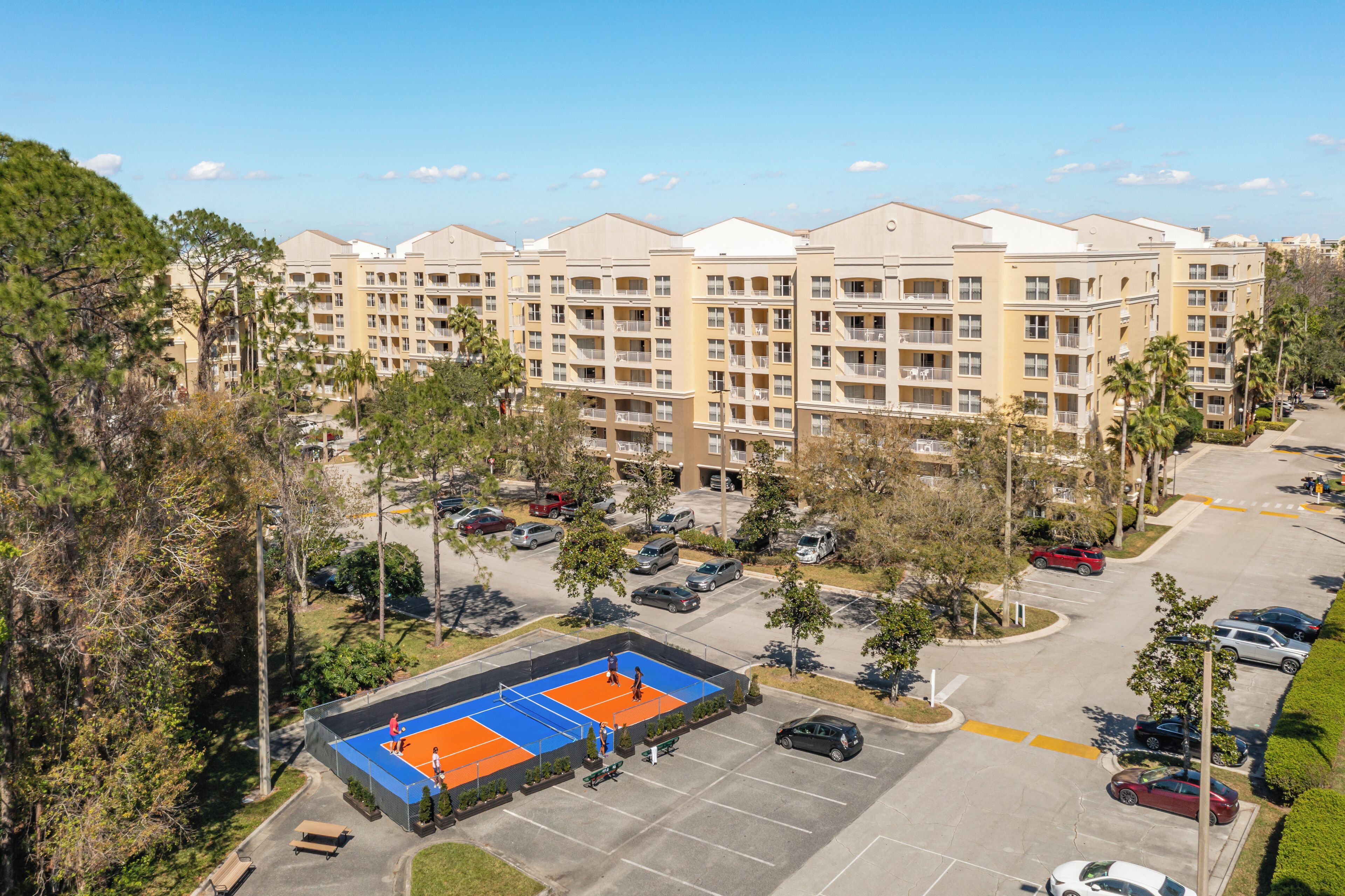 Un hotel de varios pisos con estacionamiento y cancha de tenis.