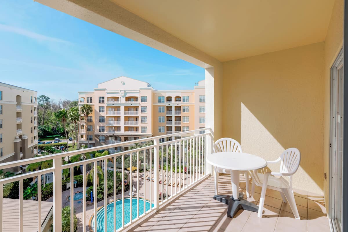 A balcony with a pool view, white chairs, and a tiled floor.