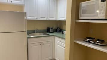 A compact kitchen with white cabinets, a stainless steel sink, a black toaster, and a microwave on a shelf.