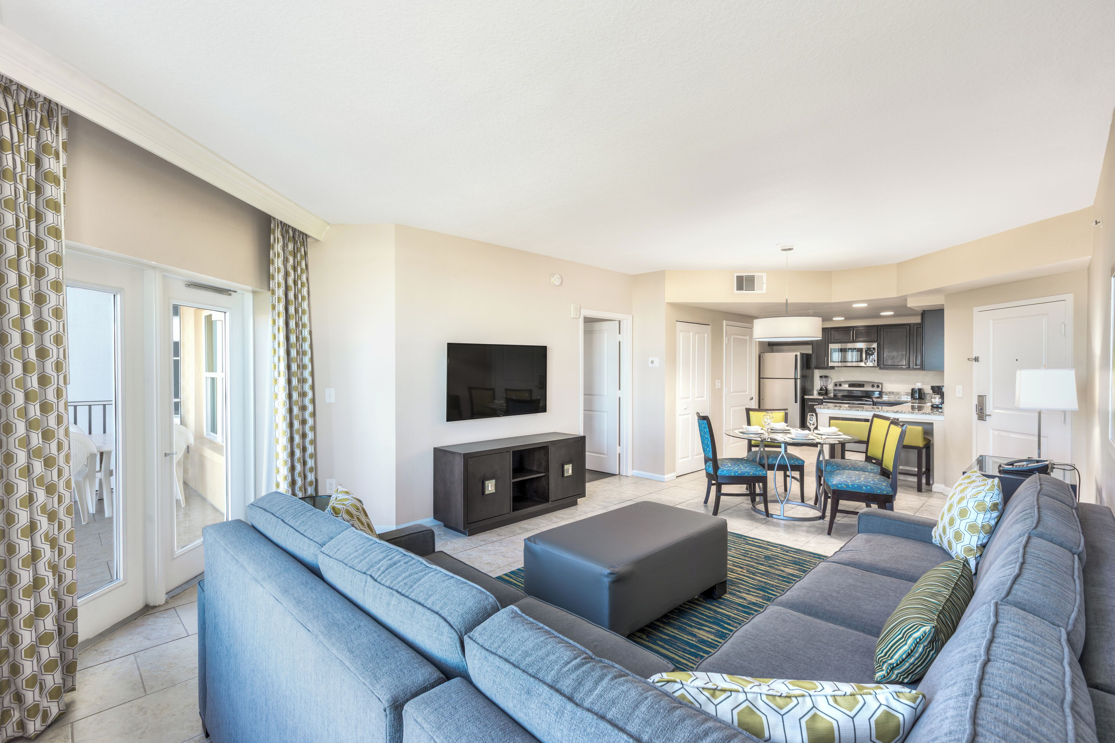 A modern living room with a sofa set, a flat-screen TV, and a dining area with chairs and a table.