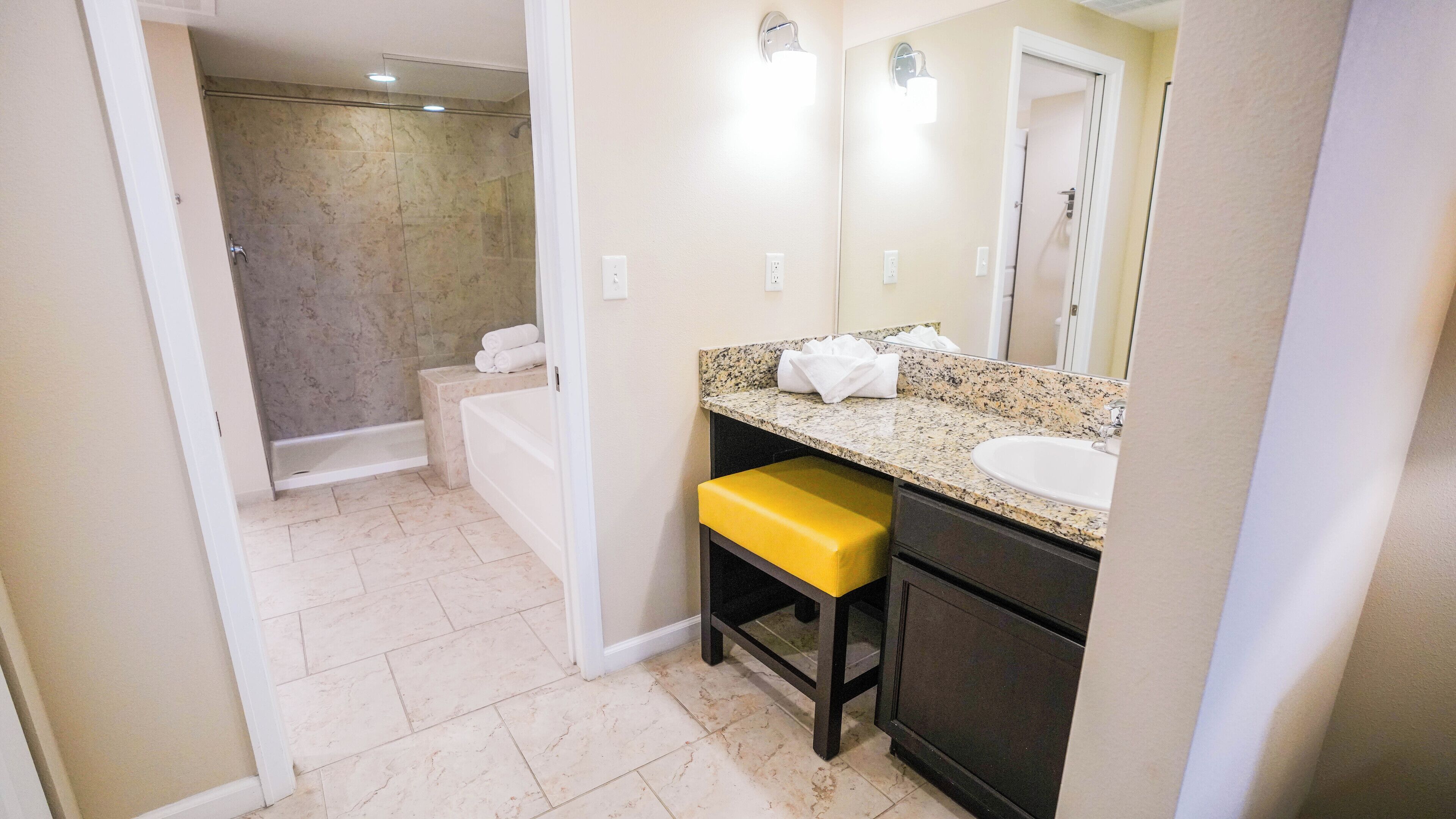 A bathroom with a bathtub, a sink, a mirror, and a yellow bench.