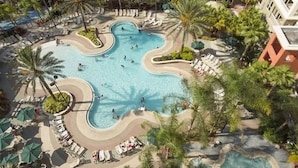 Una piscina grande y de forma irregular rodeada de sillones de descanso y palmeras.