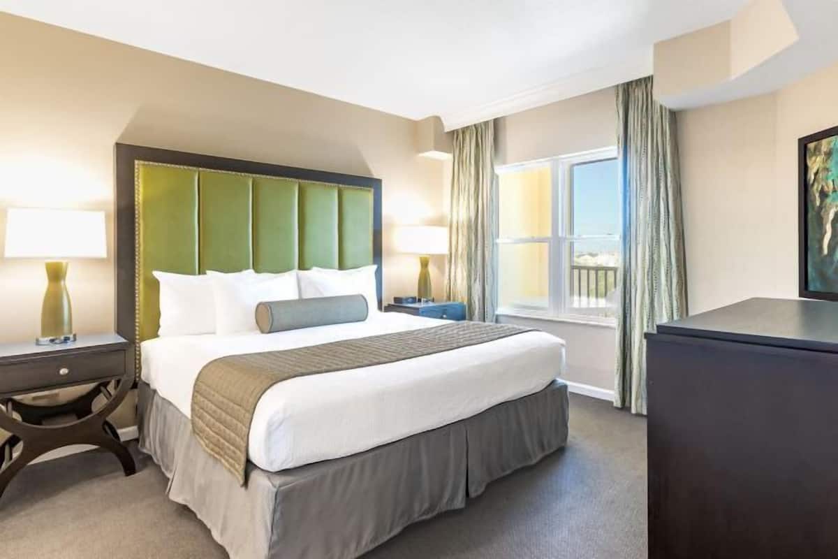 A hotel room with a large bed, a nightstand, a dresser, and a window with curtains.