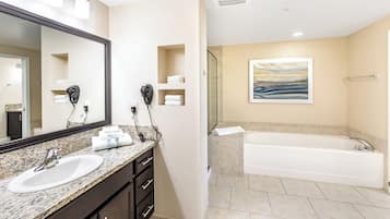 Une salle de bain moderne avec un lavabo surmonté d’un plan en granit, des meubles sombres, un grand miroir, un sèche-cheveux et un tableau accroché au mur.