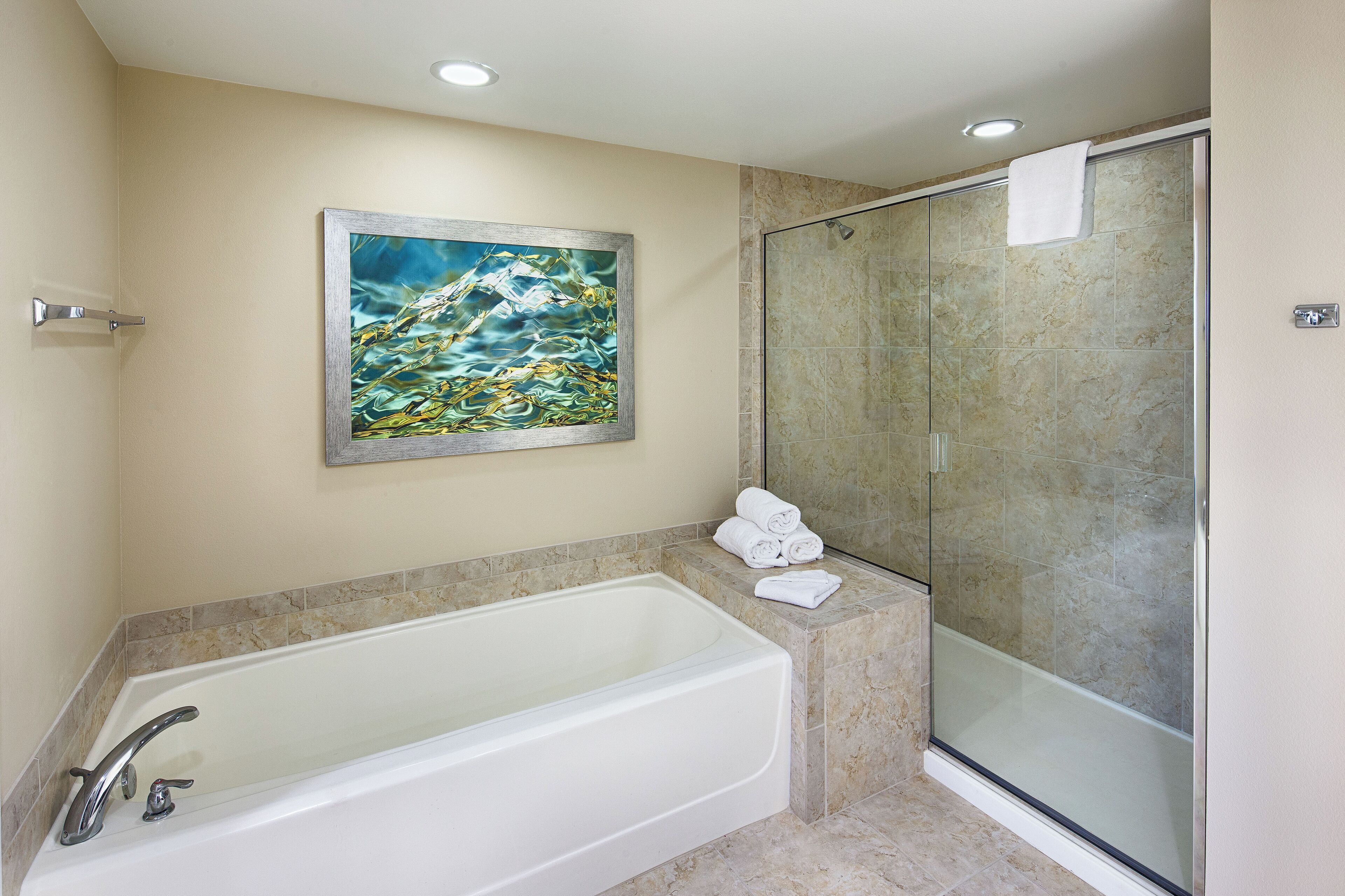A bathroom with a bathtub, a glass shower enclosure, and a painting on the wall.