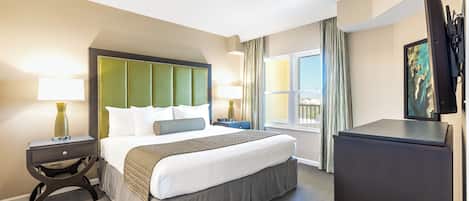 A hotel room with a large bed, a nightstand with a lamp, a dresser, and a window with curtains.