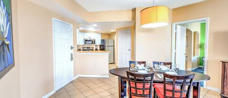 A dining area with a round table and chairs, a kitchen in the background, and a hallway leading to other rooms.