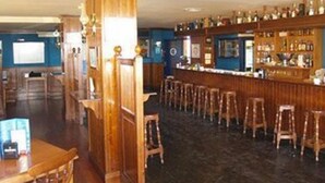 A bar area with wooden furniture, a counter with bottles, and stools. - Rocamar (La Linea de la Concepcion)