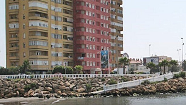 A multi-story residential building with balconies, a white fence, and a rocky shoreline. - Rocamar (La Linea de la Concepcion)