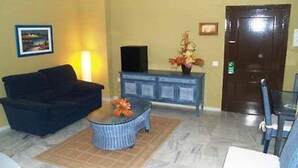 A living room with a sofa, a coffee table, a television, and a door. - Rocamar (La Linea de la Concepcion)