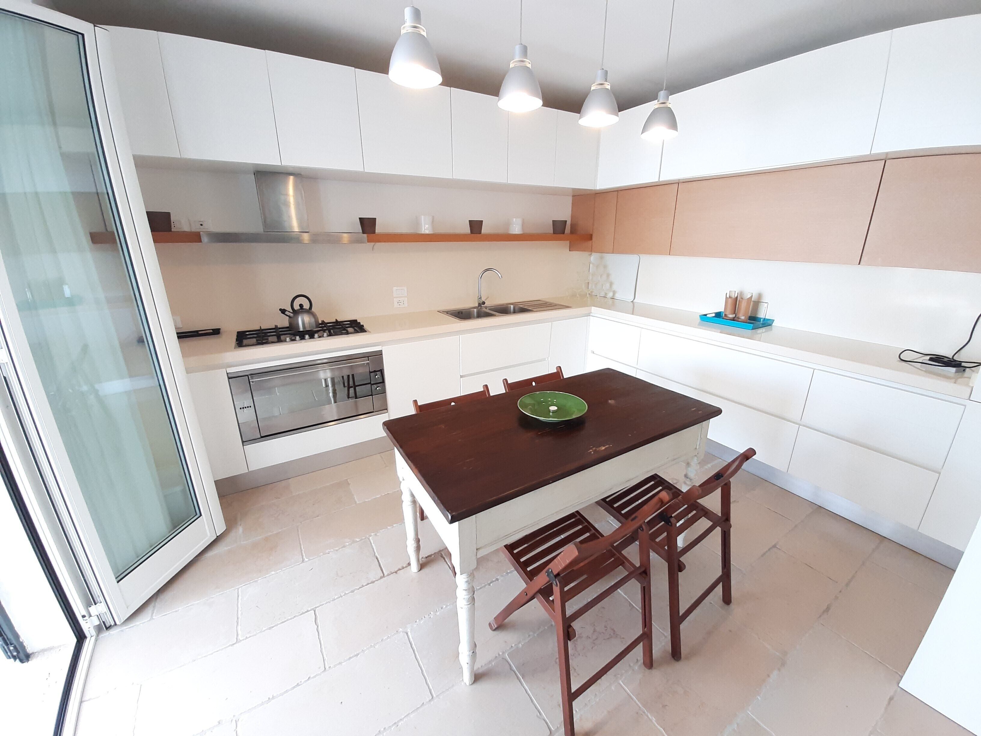 A modern kitchen with white cabinets, a wooden table, and a gas stove.