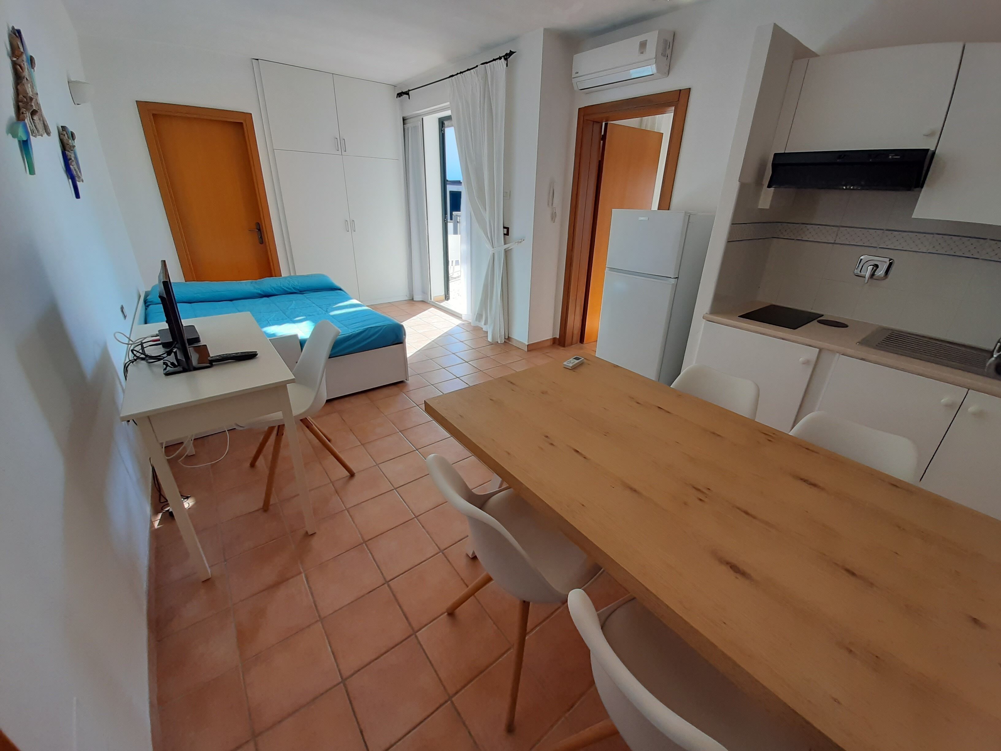 Una habitación pequeña con cama, escritorio y kitchenette.