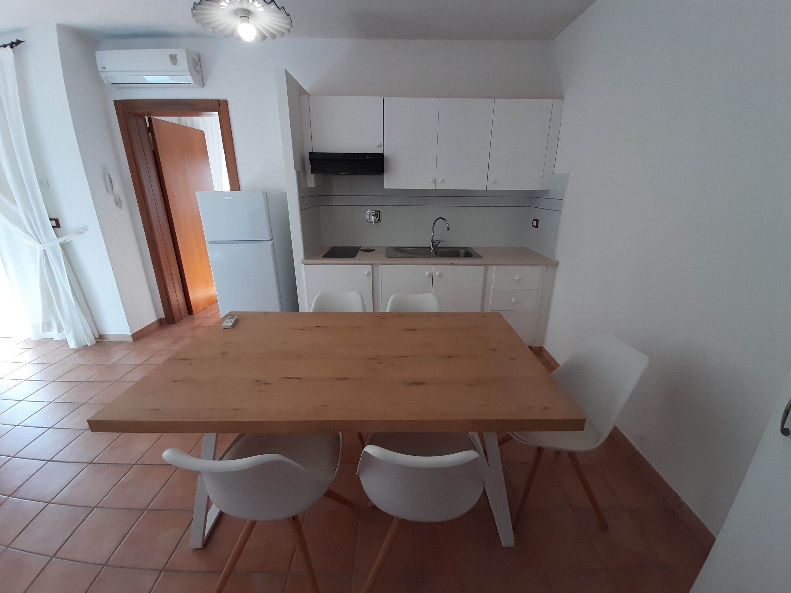 Een kleine keuken met witte kastjes, een houten tafel en twee witte stoelen.