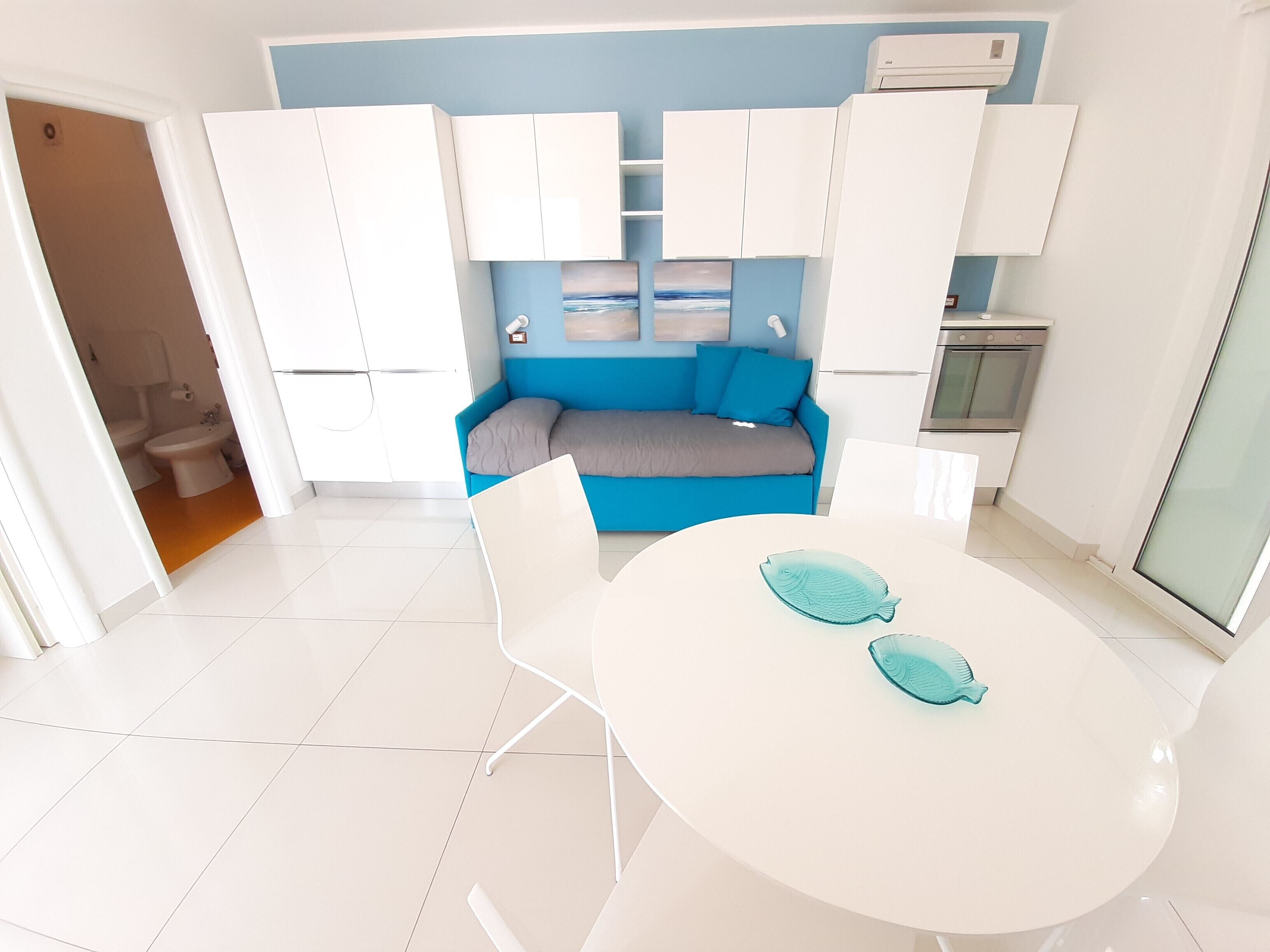 A modern kitchen with white cabinets, a blue sofa, and a round table with two fish-shaped coasters.
