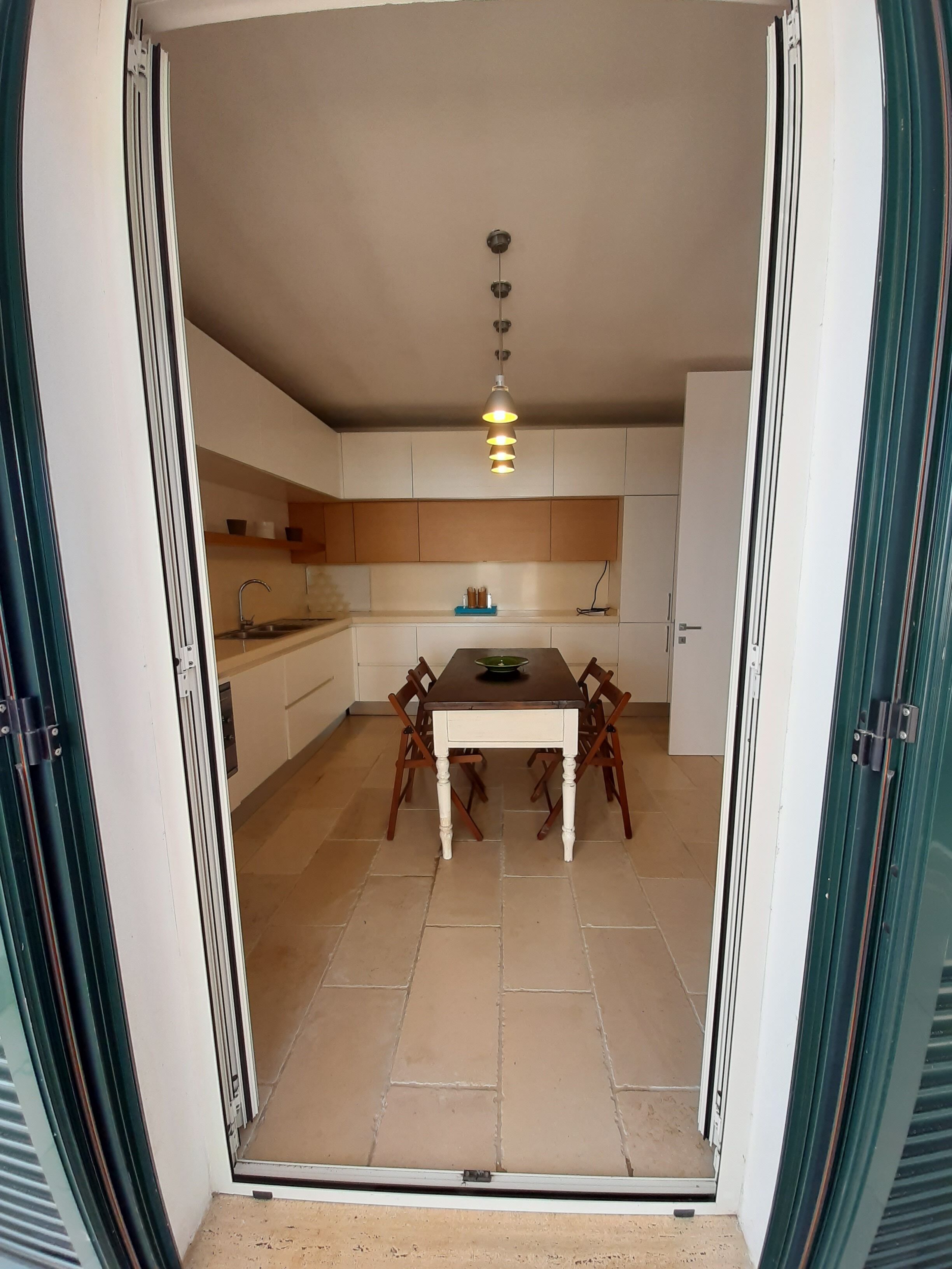 Een moderne keuken met een eettafel, stoelen, een hanglamp en keukenkastjes.