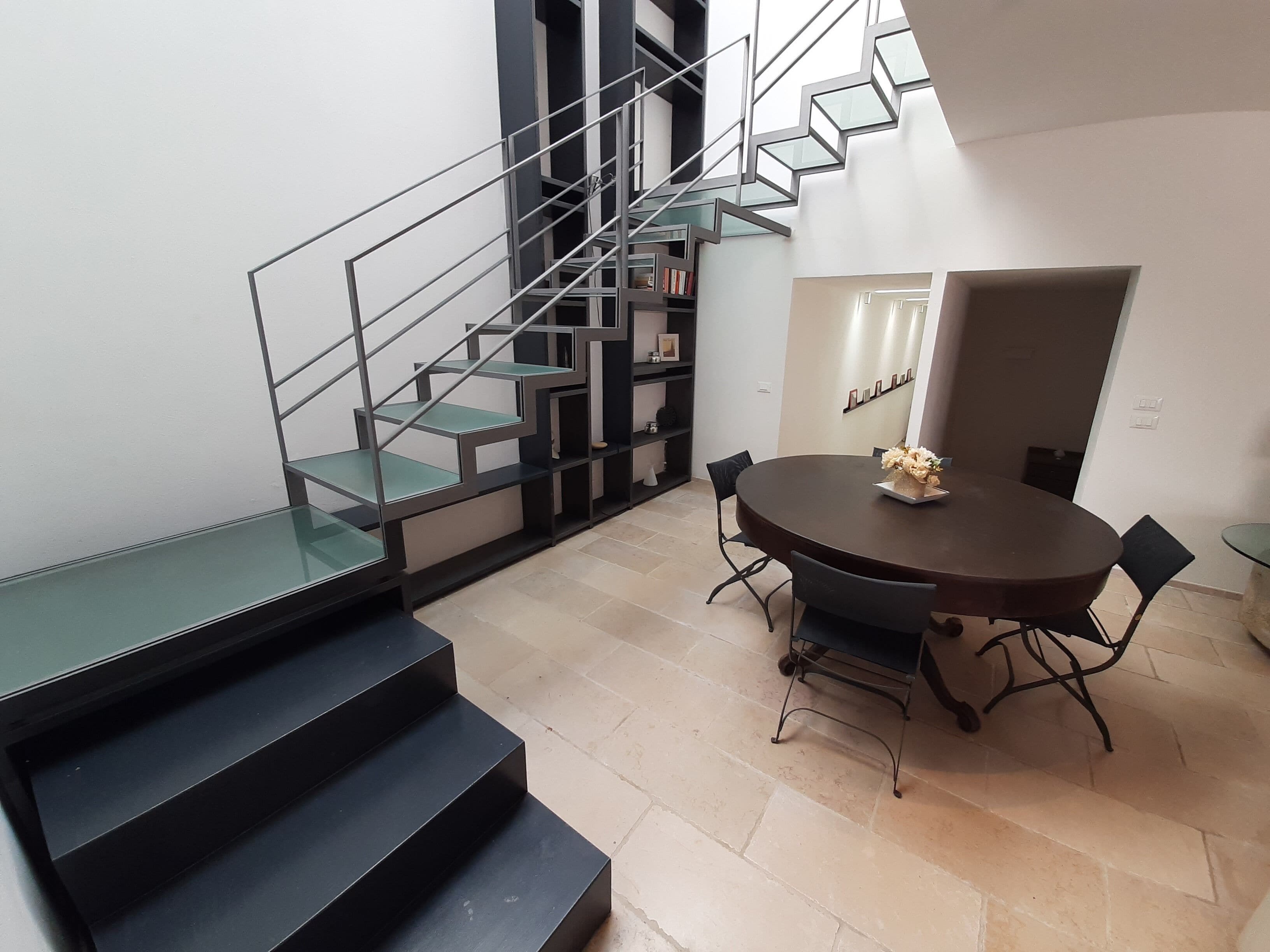 Un interno moderno con una scala, un'area pranzo con un tavolo rotondo e una libreria.