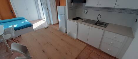 A compact kitchen with a wooden table, white chairs, a sink, and a refrigerator.